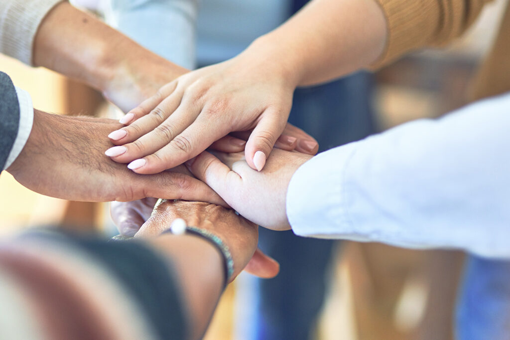 Hände die aufeinander gelegt wurden von mehreren Personen und Zusammenhalt darstellen.